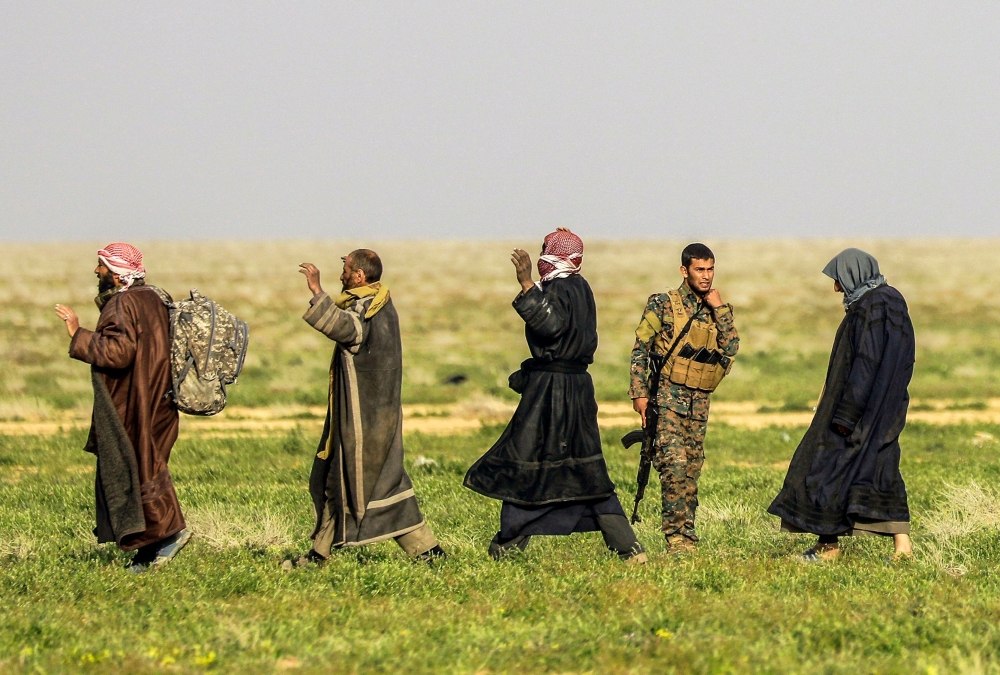 A fighter with the US-backed Syrian Democratic Forces (SDF) stands guard as people queue at a scanning area for those who are evacuated from the Islamic State (IS) group's embattled holdout of Baghouz, during an operation to expel IS jihadists from the ar
