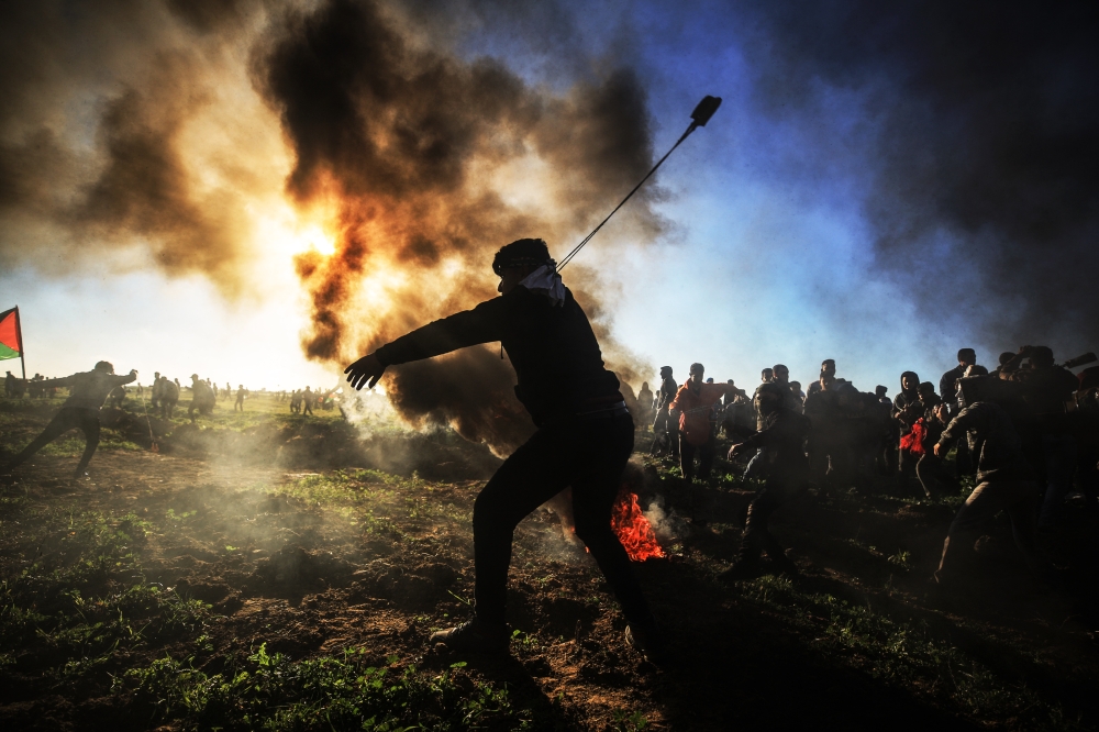 Palestinian throws a stone with a slingshot towards Israeli security forces during the 