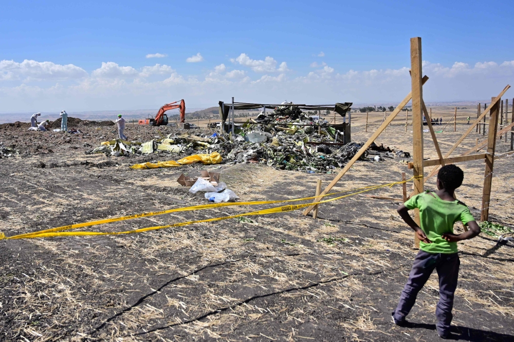 A boys look as forensic investigators comb the ground for DNA evidence near a pile of twisted airplane debris at the crash site of an Ethiopian airways operated Boeing 737 MAX aircraft on March 16, 2019 at Hama Quntushele village near Bishoftu in Oromia r