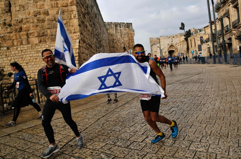 Competitors hold the Israeli flag along the Old City ramparts during Jerusalem's 9th International Marathon, on March 15, 2019. AFP / Gil Cohen-Magen 