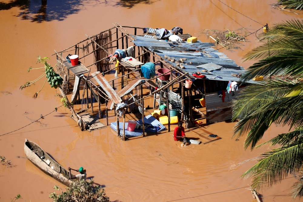 A local paddles past a woman at her home during floods after Cyclone Idai, in Buzi district, outside Beira, Mozambique, March 21, 2019. REUTERS/Siphiwe Sibeko