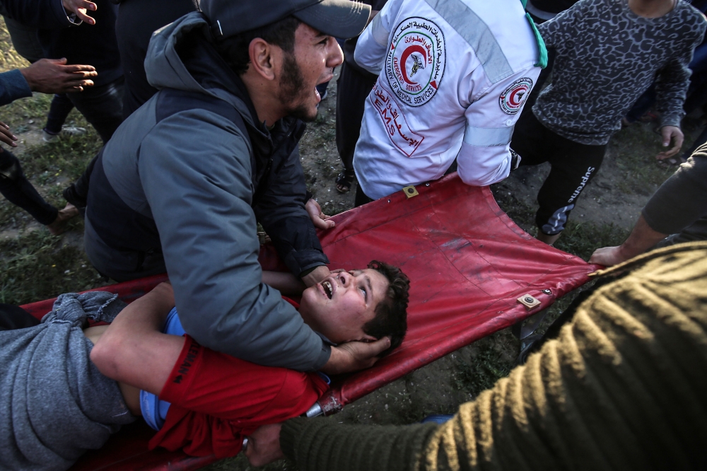 A Palestinian man carries an injured youth at the border fence with Israel east of Gaza City on March 22, 2019. AFP/Said Khatib 