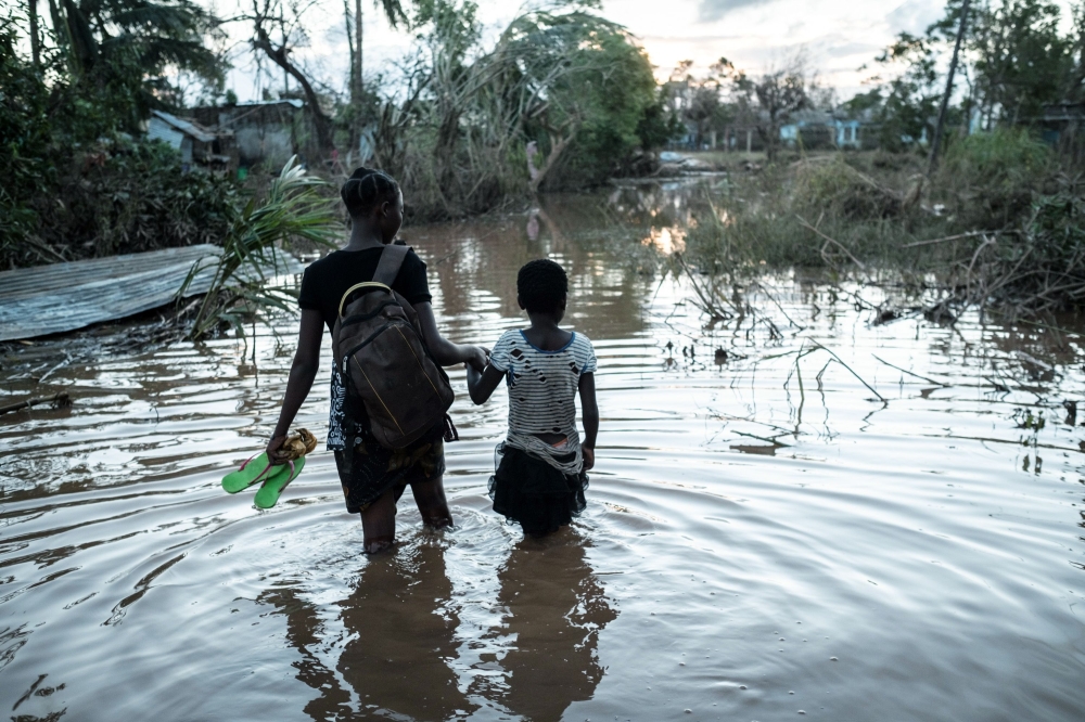 Rosita Moises Zacarias (L), 15, holding the hand of her sister Joaninha Manuel, 9, walks in flooded waters from their house destroyed by the cyclone Idai, to go to seep in a shelter in Buzi, Mozambique, on March 22, 2019.  AFP / Yasuyoshi CHIBA
