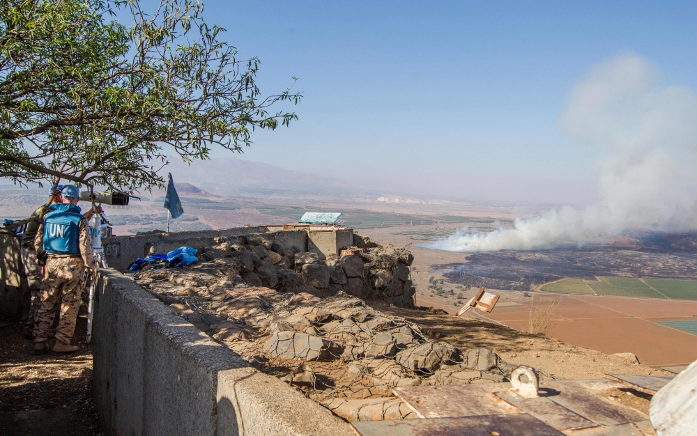 FILE PHOTO:  Members of the United Nations Disengagement Observer Force Zone (UNDOF) using a binocular to look towards the Syrian side of the Golan Heights as smoke billows during clashes between forces loyal to Syrian President Bashar Assad and rebels ov