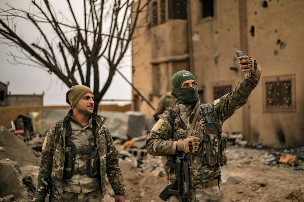 Members of the Syrian Democratic Forces (SDF) use a cell phone to take a 