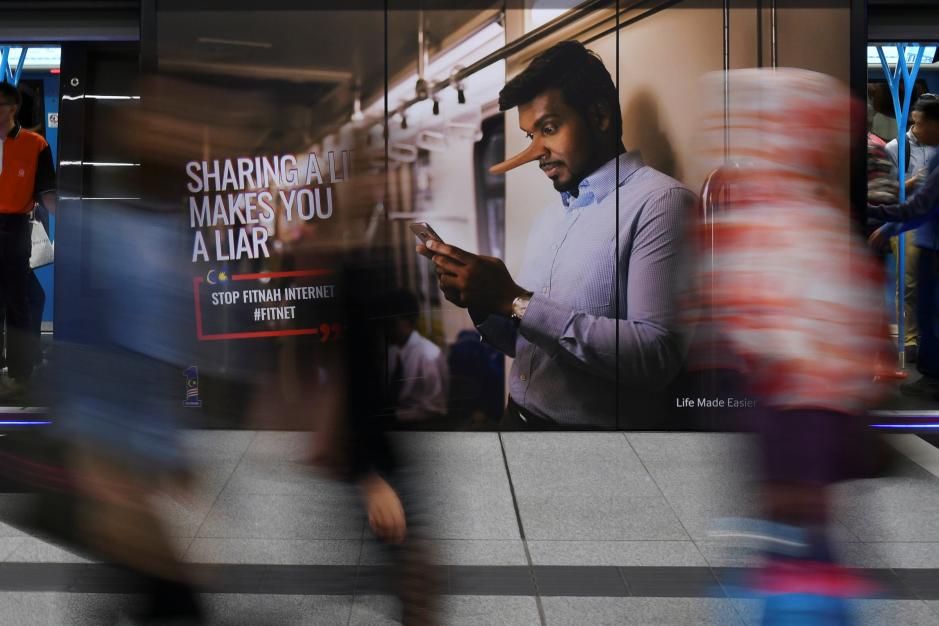 Commuters walk past an advertisement discouraging the dissemination of fake news at a train station in Kuala Lumpur, Malaysia, March 28, 2018. (Reuters) 