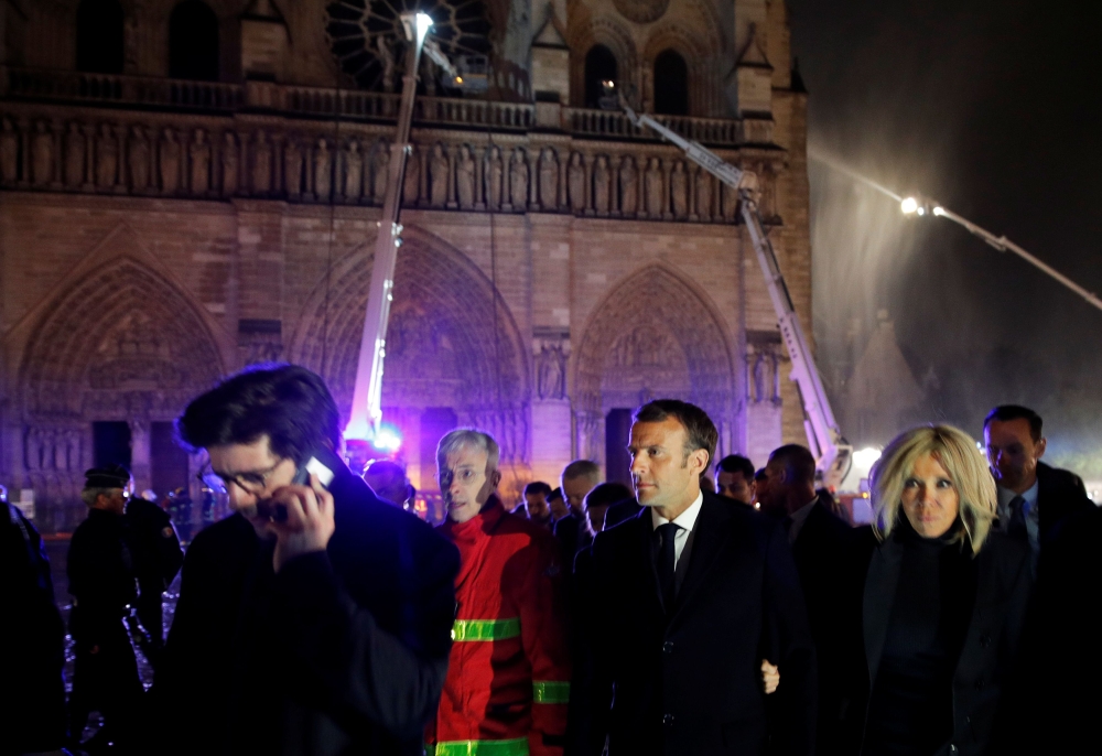 French President Emmanuel Macron and his wife Brigitte walk outside the Notre Dame Cathedral where a fire continues to burn in Paris on April 16, 2019.  AFP / Pool / Philippe Wojazer 