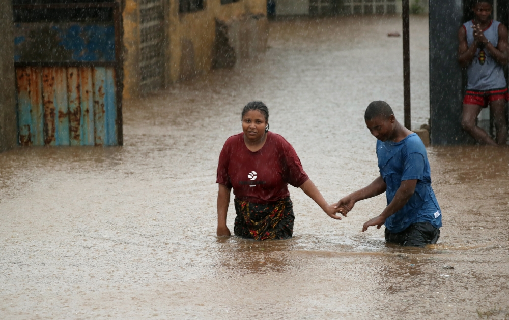 A man helps a woman through a flooded neigbourhood in the aftermath of Cyclone Kenneth in Pemba, Mozambique, April 28, 2019. REUTERS/Mike Hutchings