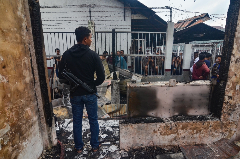 An armed plainclothes policeman (L) secures the area around Siak prison in Siak Sri Indrapura in Riau province on May 11, 2019 after rioting and a fire broke out at the detention centre leading to a prison break. AFP / WAHYUDI