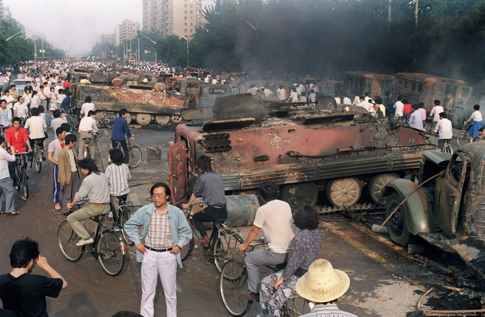 In this file photo taken on June 4, 1989, residents gather near the smoking remains of over 20 armoured personnel carriers burnt by demonstrators during clashes with soldiers near Tiananmen Square in Beijing.  AFP / Manny Ceneta 