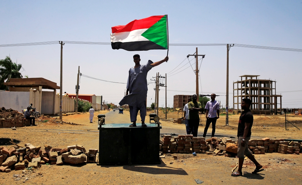 A Sudanese protester holds a national flag as he stands on a barricade along a street, demanding that the country's Transitional Military Council hand over power to civilians, in Khartoum, Sudan June 5, 2019. Reuters
