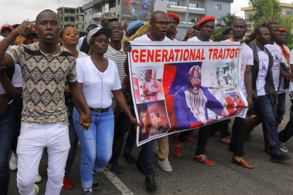 People carry a banner depicting Liberia's President George Weah as they march during a protest to voice discontent towards the presidency of Weah, whose policies they see as having failed to curb economic decline and mitigate corruption, in Monrovia, Libe