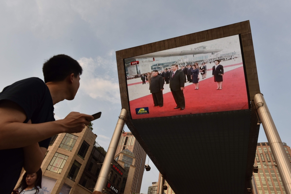 A man watches news footage of Chinese President Xi Jinping (R) being greeted in Pyongyang by North Korean leader Kim Jong Un, on a large screen outside a shopping mall in Beijing on June 20, 2019.(AFP / GREG BAKER)