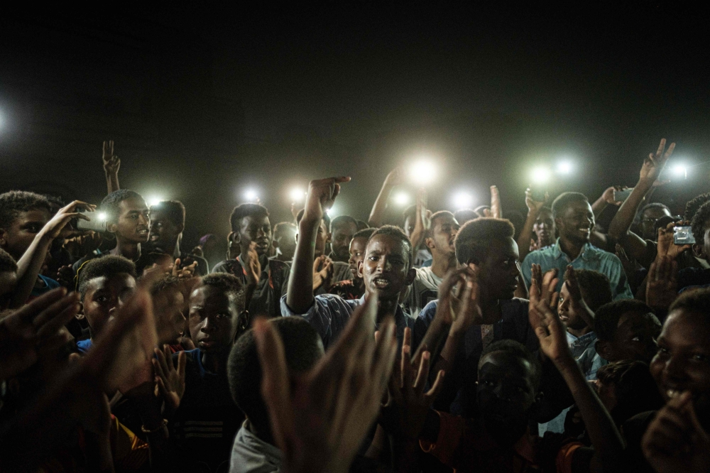 People chant slogans as a young man recites a poem, illuminated by mobile phones, before the opposition's direct dialog with people in Khartoum on June 19, 2019.   AFP / Yasuyoshi CHIBA