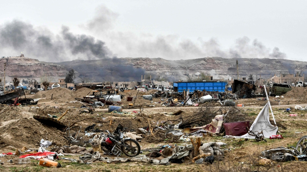 In this file photo taken on March 24, 2019, smoke rises behind destroyed vehicles and damaged buildings in the village of Baghouz in Syria's eastern Deir Ezzor province near the Iraqi border, a day after the Islamic State (IS) group's 