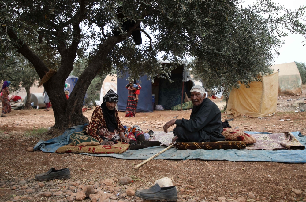 In this file photo taken on June 04, 2019, an elderly Syrian couple sits under an olive tree at a DIP camp for Interally Displaced Persons near the town of Aqrabat in Syria's northern Idlib province, as Muslims around the world celebrate Eid al-Fitr, the 