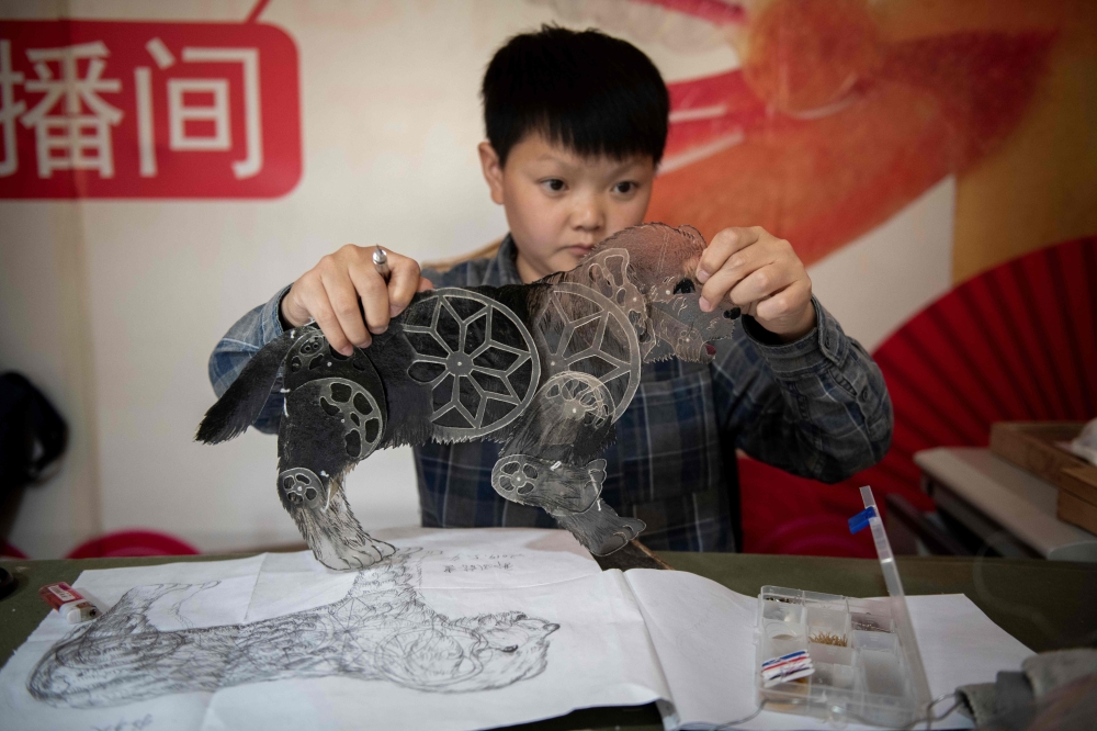 Jin Xinchun, a member of the Flying Dragon Troupe, creates a shadow puppet at the troupe's studio on the outskirts of Beijing. AFP / NICOLAS ASFOURI