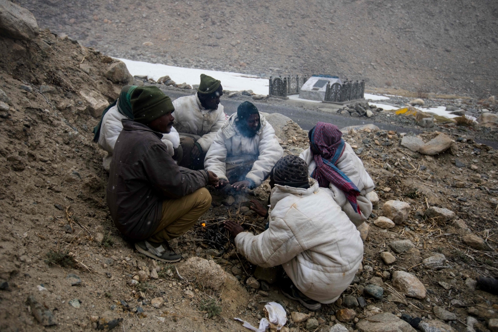 In this picture taken on May 18, 2019, road maintenance workers from India's low-lying eastern Jharkhand state warm up around a bonfire during a inclement weather while working along Pangong Lake road near the Chang La pass in northern India's Ladakh regi