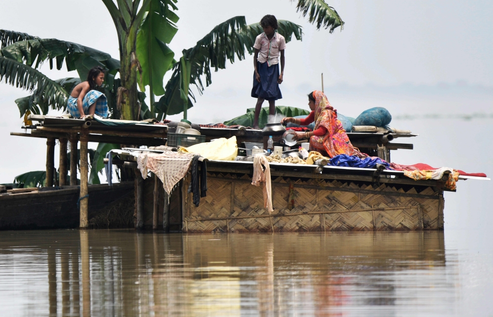 Members of an Indian family stand atop a hut at the flood affected area of Hatishila in Kamrup district of India's Assam state on July 16, 2019. AFP / Biju BORO