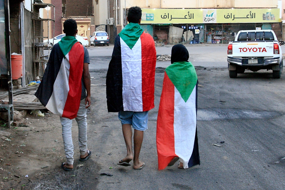 Sudanese demonstrators wear their national flag as they celebrate in Khartoum early on August 3, 2019, after Sudan's ruling generals and protest leaders reached a 