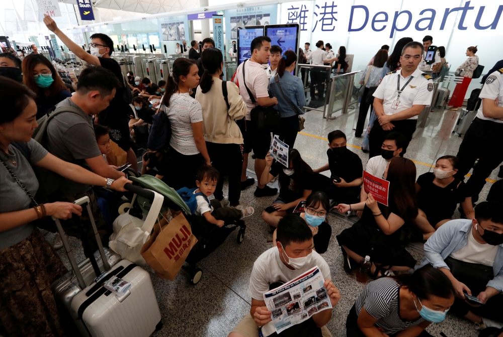 Passengers walk past anti-government protesters sitting on the floor in front of security gates during a demonstration at Hong Kong Airport, China August 13, 2019. REUTERS/Issei Kato