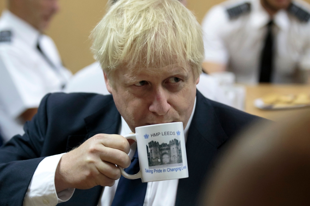 Britain's Prime Minister Boris Johnson drinks from a HMP Leeds prison mug as he talks with prison staff during a visit to HM Prison Leeds, a Category B men's prison in Leeds, northern England, on August 13, 2019. / AFP / POOL / Jon Super