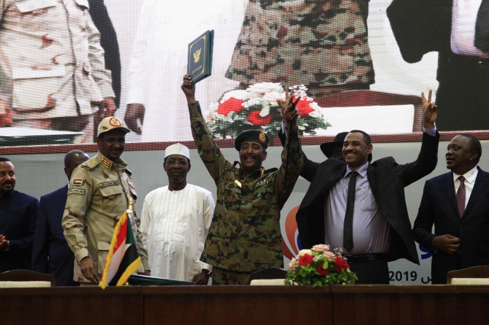 Sudan's protest leader Ahmad Rabie (2nd-R), flashes the victory gesture alongside General Abdel Fattah al-Burhan (C), the chief of Sudan's ruling Transitional Military Council (TMC), during a ceremony where they signed a 