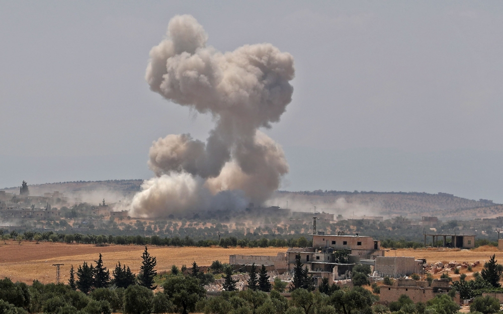 Smoke billows above buildings during a reported air strike by pro-regime forces near the town of Hish in Syria's Idlib province on August 19, 2019.