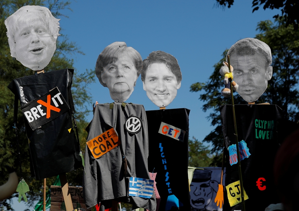 Protesters hold cutout portraits of Britain's Prime Minister Boris Johnson, German Chancellor Angela Merkel, Canada’s Prime Minister Justin Trudeau and French President Emmanuel Macron during an anti-G7 protest march on the French-Spanish border, in Henda