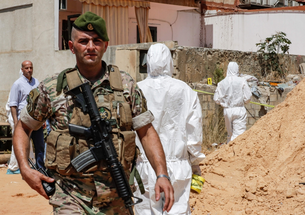 A Lebanese army soldier walks past military intelligence forensic investigators of inspecting the scene where two drones came down in the vicinity of a media centre of the Shiite Hezbollah movement earlier in the day, in the south of the capital Beirut on