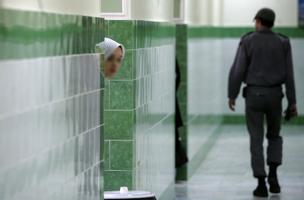 (FILES) In this file photo taken on June 13, 2006 an Iranian inmate peers from behind a wall as a guard walks by at the female section of the infamous Evin jail, north of Tehran. AFP / ATTA KENARE