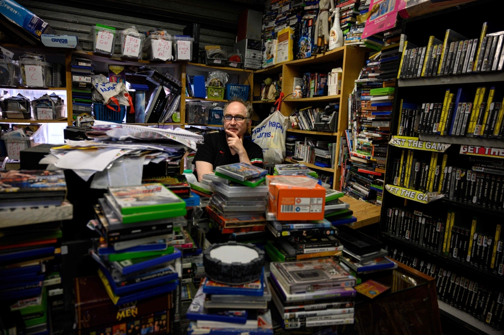 A shopkeeper sits amongst his stock of films and video games at his stall on Peterborough Market in Peterborough city centre, central England on September 26, 2019. AFP / Oli Scarff