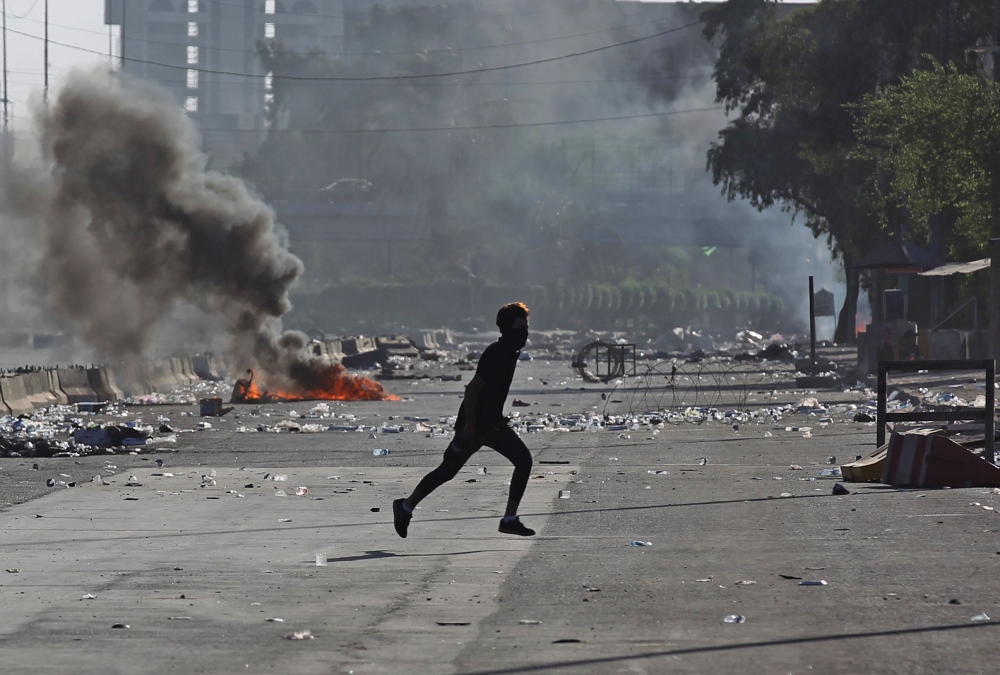 An Iraqi protester runs amidst clashes during a demonstration against state corruption, failing public services, and unemployment in the Iraqi capital Baghdad's central Khellani Square on October 4, 2019. / AFP / AHMAD AL-RUBAYE
