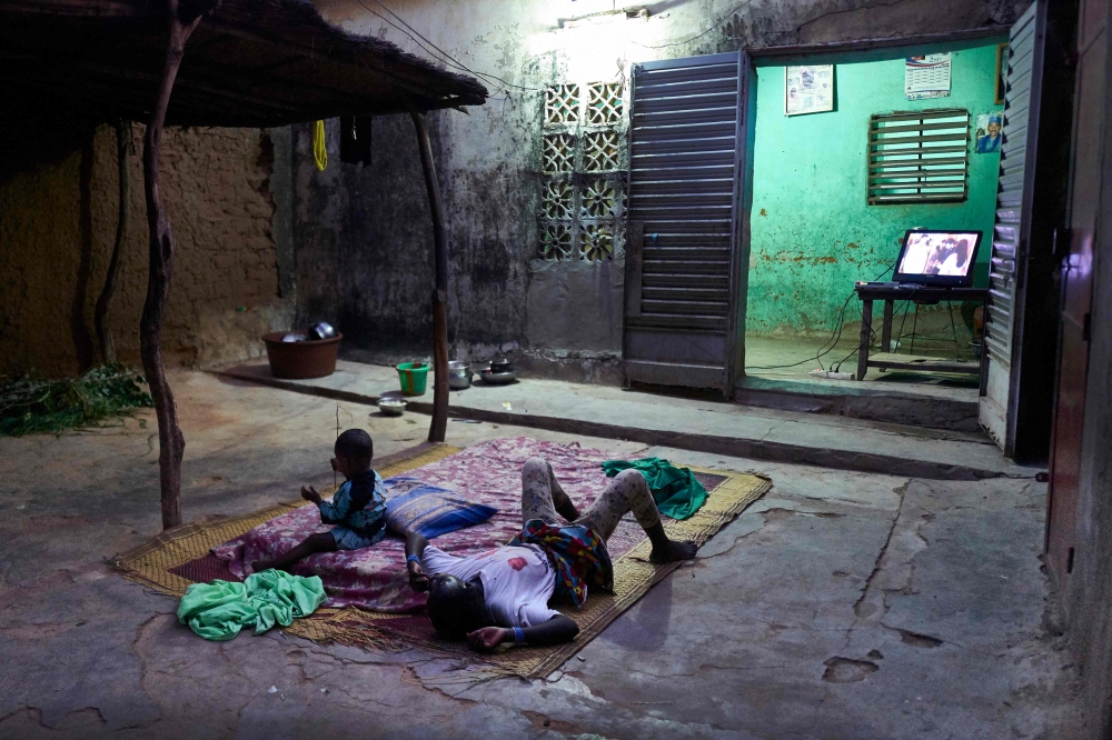 Two displaced children lie down to watch the television in the court of a house in Segou on September 30, 2019.  AFP / Michele Cattani 