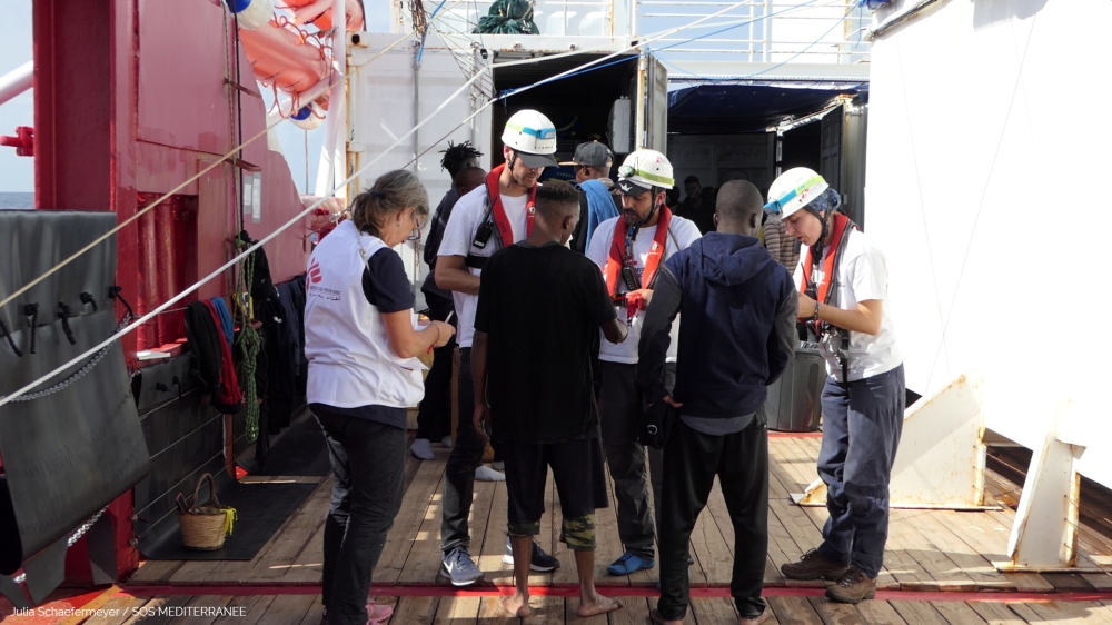 Members of Doctors Without Borders (MSF) talk to migrants onboard Ocean Viking after a rescue operation, October 13, 2019.  Julia Schaefermeyer/SOS Mediterranee via Reuters. 