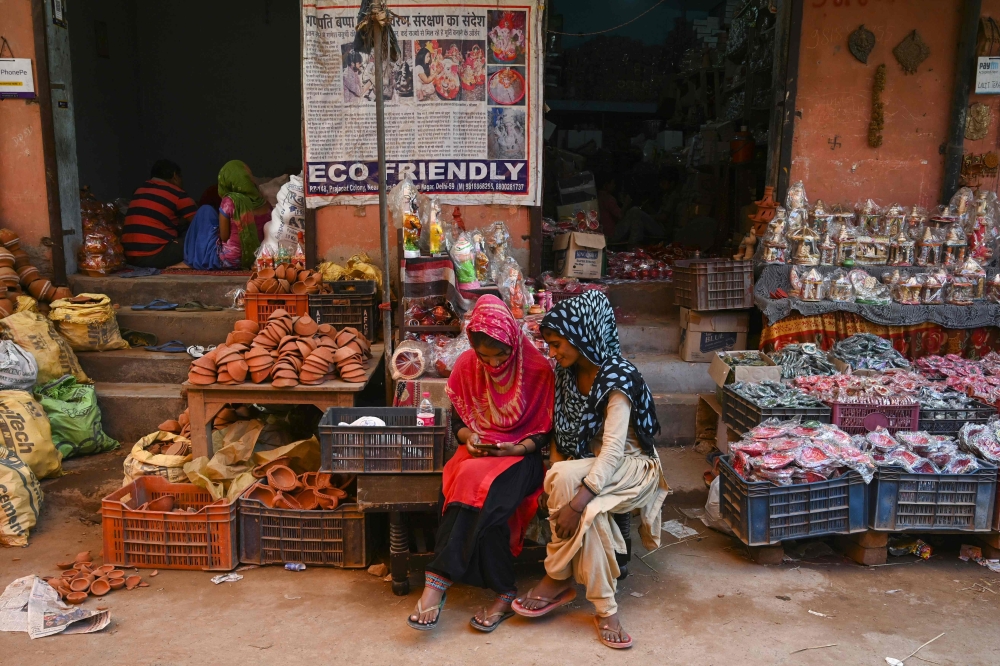 In this photograph taken on October 4, 2019, women use a mobile phone as they sit outside their shop displaying items made of clay, at Kumhar Gram (Potter's Village) in New Delhi. AFP / Money Sharma
 