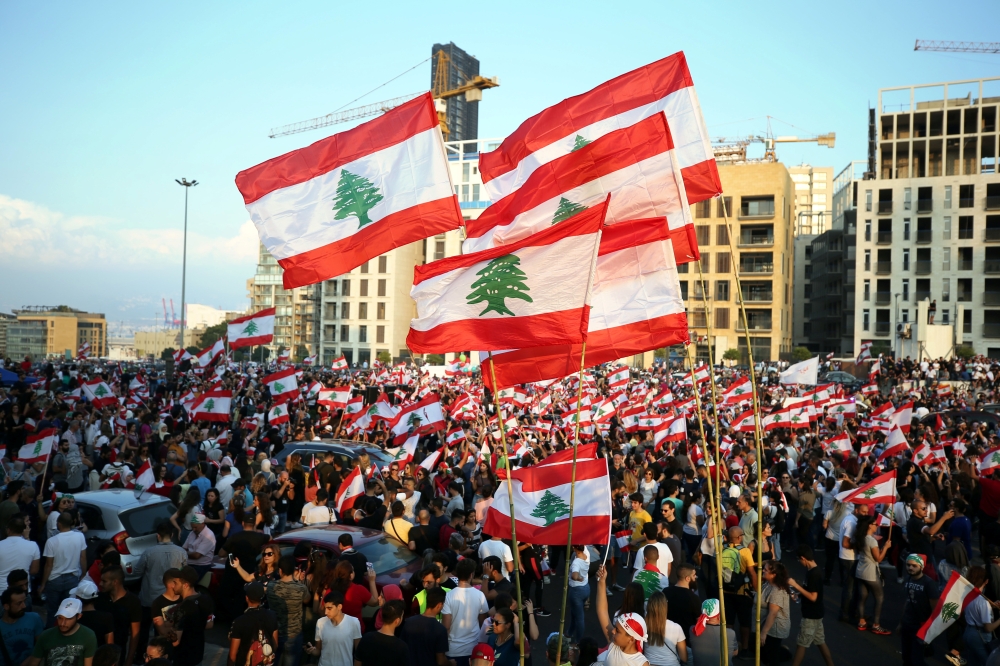 Demonstrators carry national flags during an anti-government protest in downtown Beirut, Lebanon October 20, 2019. REUTERS/Ali Hashisho