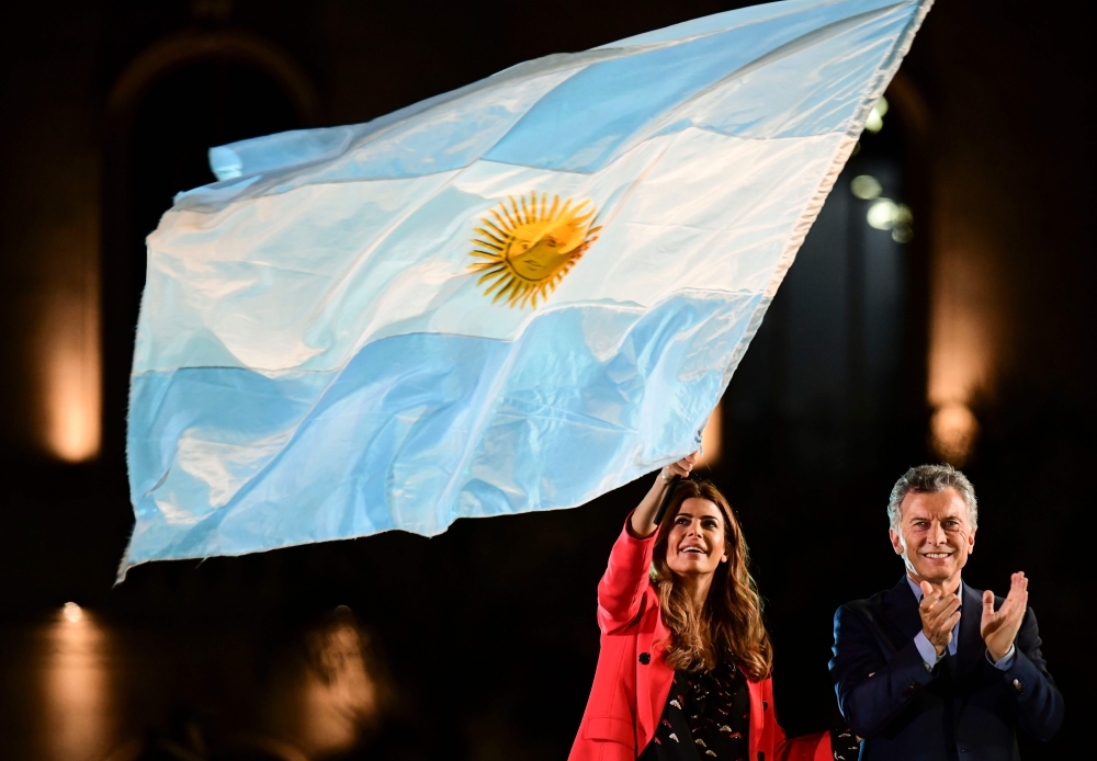 Argentina's President and presidential candidate of the Juntos por el Cambio party, Mauricio Macri (R), applauds as First Lady Juliana Awada was a national flag during the closing rally of his campaign in Cordoba, Argentina, on October 24, 2019. Argentina