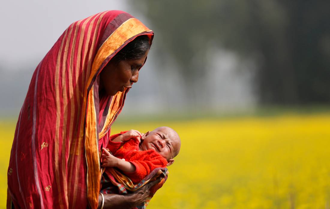 A woman holds a baby as she walks through a mustard field on the outskirts of Dhaka January 22, 2014. Reuters/Andrew Biraj 