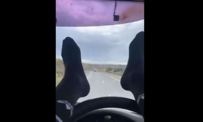 The two-and-a-half minute clip shows the driver with both feet in long black socks on the steering wheel navigating with his calves on the slow lane of a two-lane highway with apparent ease