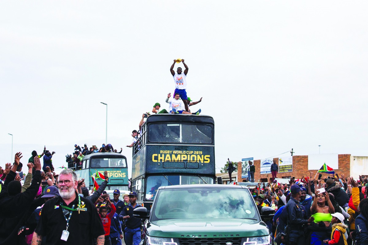 People cheer as South African Rugby captain Siya Kolisi (C) holds up the Web Ellis Trophy while the South African Rugby World Cup winner team parades on an open top bus through the streets of the city of Zwide , Port Elizabeth, on November 10, 2019. AFP /