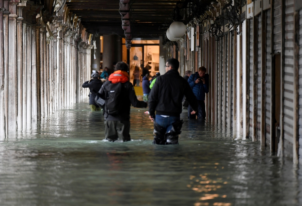 People wade through water under arcades at St. Mark's Square during high tide in Venice, Italy November 17, 2019. REUTERS/Alberto Lingria
