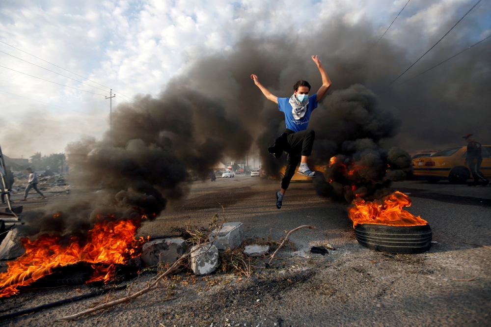 A protester jumps between burning tires during ongoing anti-government protests in Basra, Iraq November 24, 2019. Reuters/Essam al-Sudani