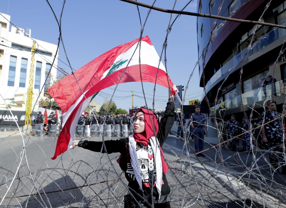 A Lebanese demonstrator waves the national flag while security forces stand by, during an anti-American protest near the US embassy in Awkar, northeast of the capital Beirut, on November 24, 2019. AFP / Anwar Amro
