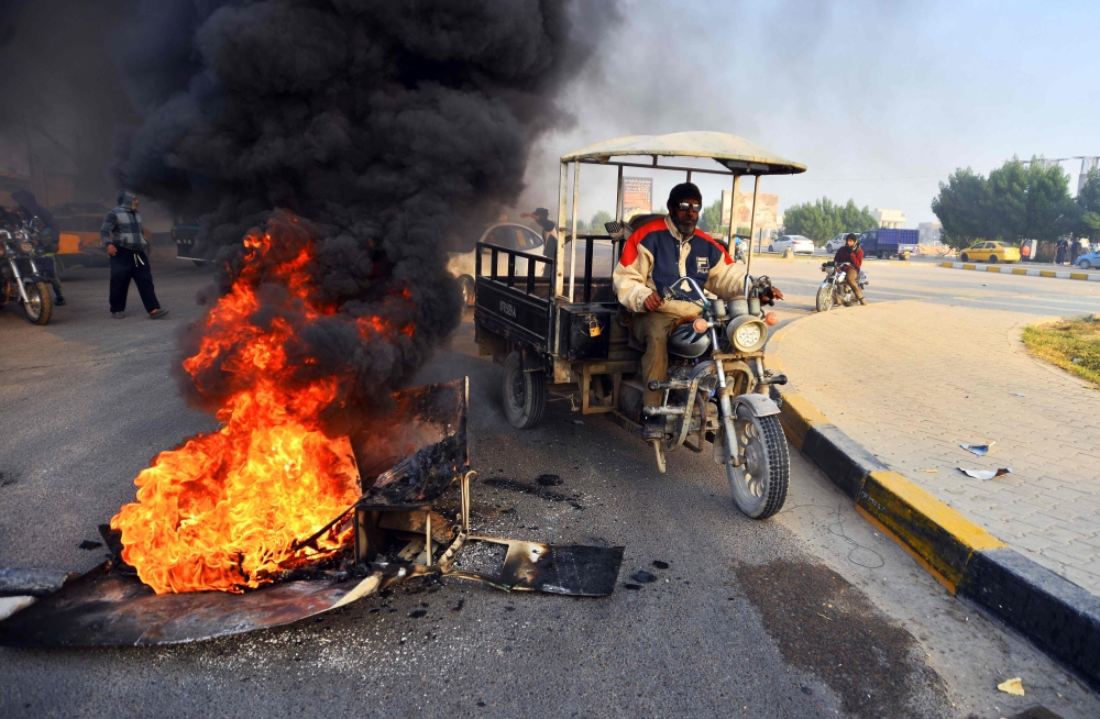 Iraqis walk past burning tyres at a roadblock in the central holy shrine city of Najaf on November 27, 2019, amid ongoing anti-government demonstrations.  AFP / Haidar HAMDANI