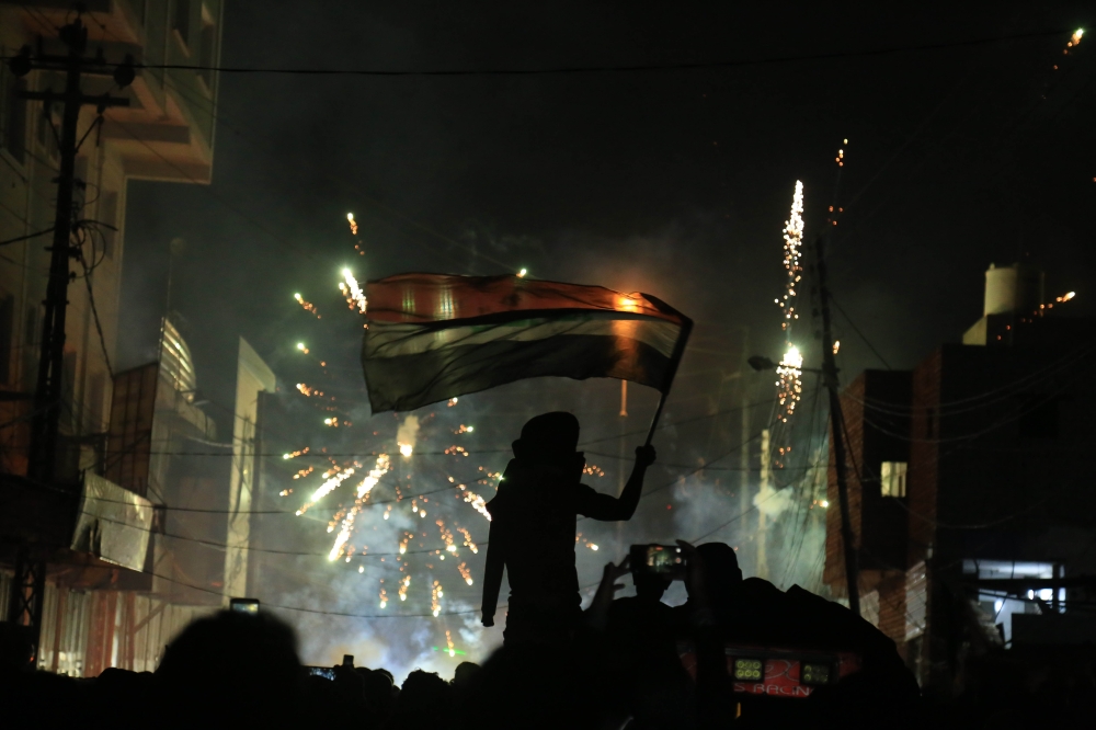 An Iraqi demonstrator waving the national flag is silhouetted during clashes with security forces in the holy shrine city of Karbala on November 29, 2019, amid ongoing anti-government protests.   AFP / Mohammed SAWAF