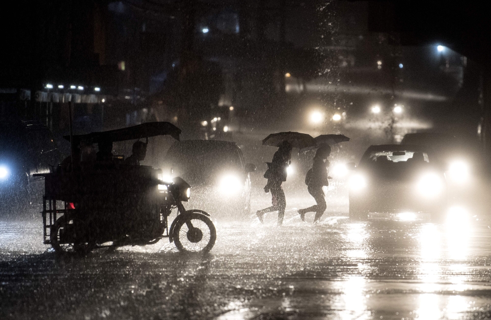 File photo: People cross a road during heavy rain caused by Typhoon Maliksi in Manila on June 10, 2018. AFP / Noel Celis