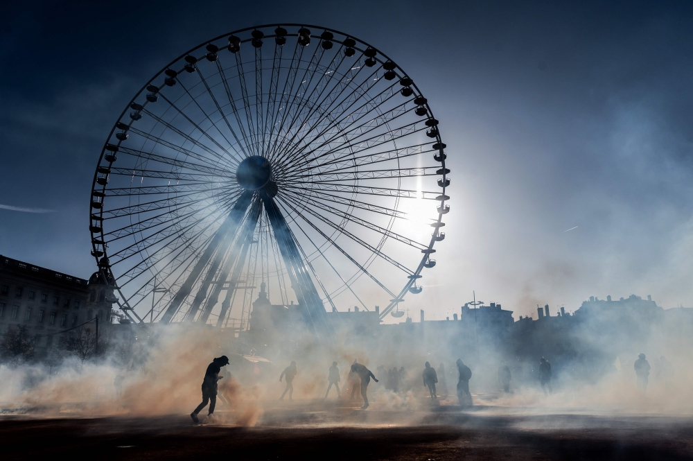 People stand amid tear-gas smoke during a demonstration on December 10, 2019 in Lyon as part of the sixth day of massive strike action over government's plans to overhaul the pension system. AFP / Jeff Pachoud
 