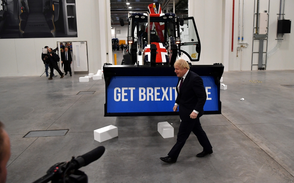 Britain's Prime Minister and Conservative leader Boris Johnson walks past a Union flag-themed JCB, with the words 
