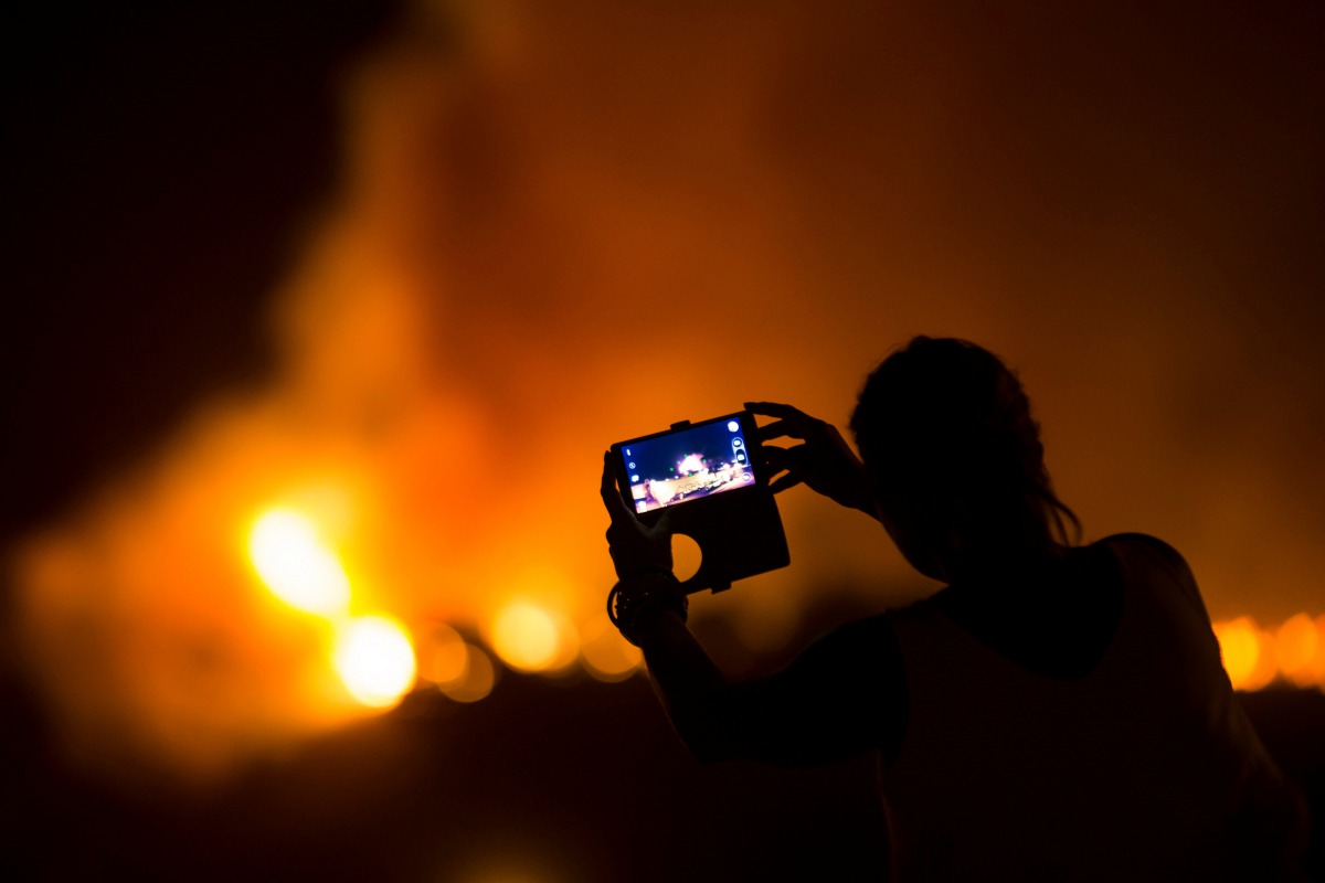 A woman uses her mobile phone to film as a forest fire in Las Manchas on the southwestern part of La Palma island, Spain, August 5, 2016. Reuters / Borja Suarez